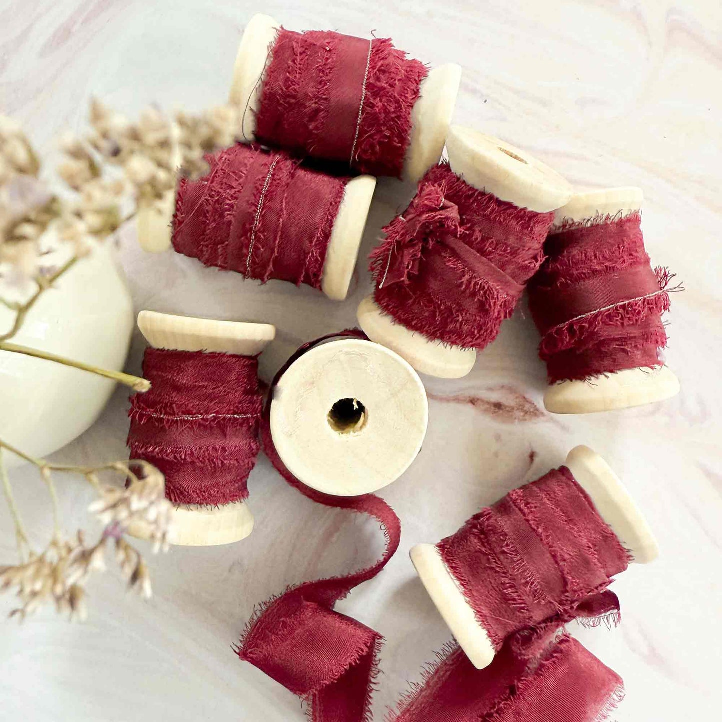Rolls of narrow burgundy silk ribbon with a raw edge