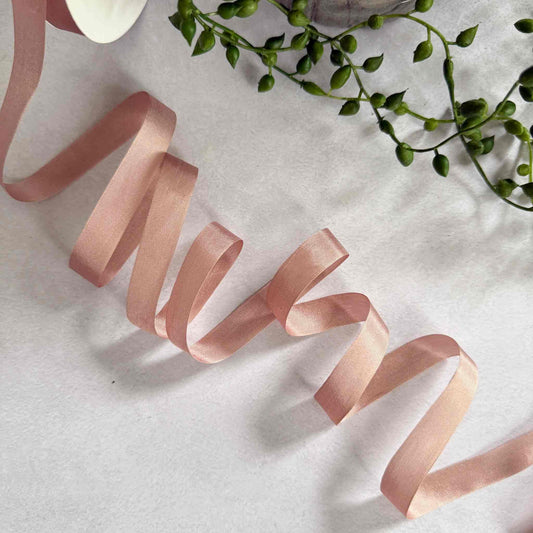 Pink ribbon on a light surface with green leaves in the corner