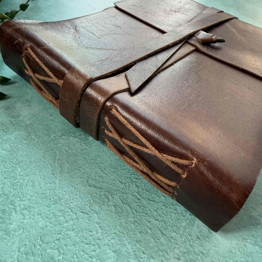 Brown leather-bound book with decorative stitching on a light green background