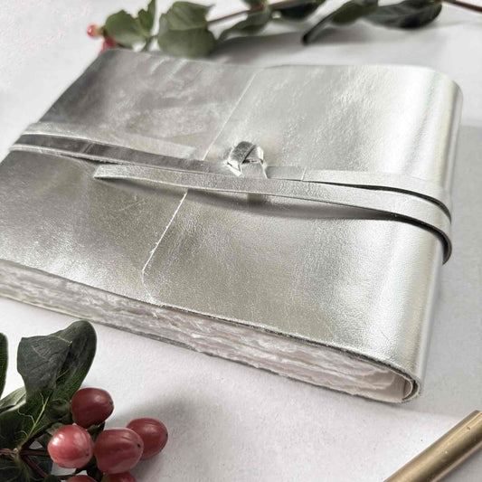 Silver clutch bag on a white surface with greenery and berries