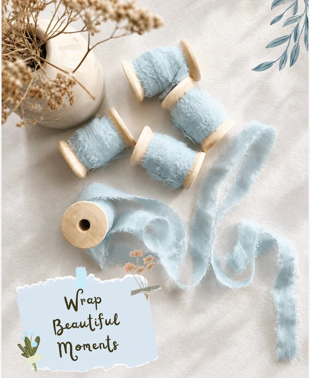 Flat-lay arrangement of soft pale blue frayed silk ribbon, 1cm wide with 5 meters per reel, presented on smooth wooden spools. One length is unfurled to display its delicate, feathered edges. Overlaid text: “Wrap Beautiful Moments”. Styled with neutral tones, dried botanicals and a ceramic vase, from The Natural Paper Company.
