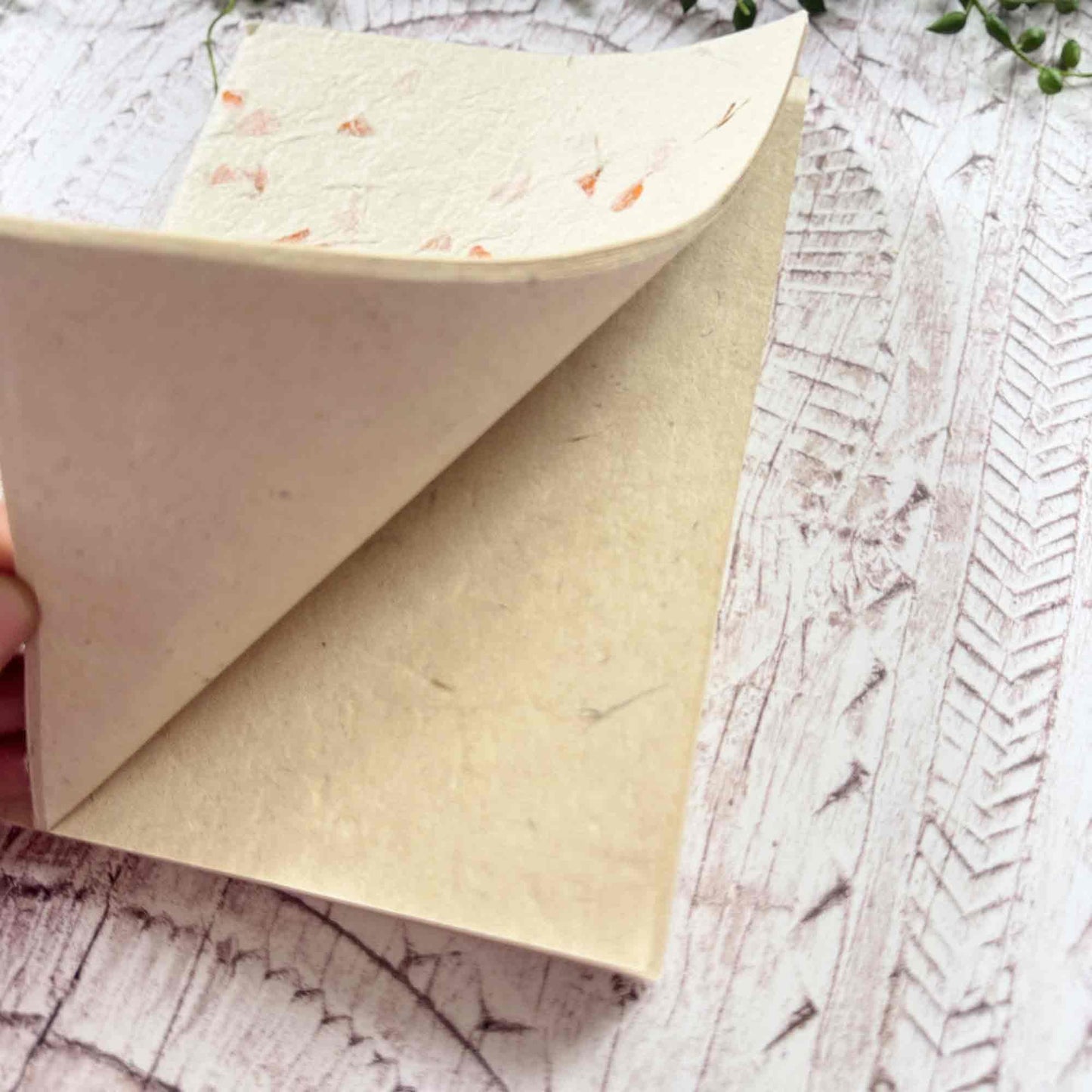 Hand opening a Marigold Lokta notebook, revealing thick, fibrous Lokta paper pages and the floral‑decorated cover