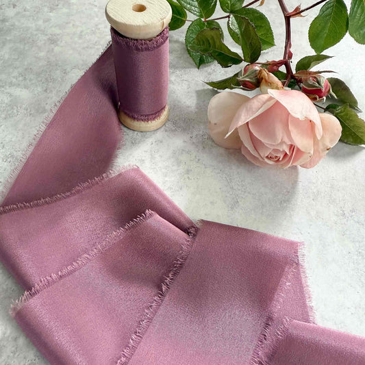 Purple fabric with frayed edges on a textured surface with a pink rose and green leaves