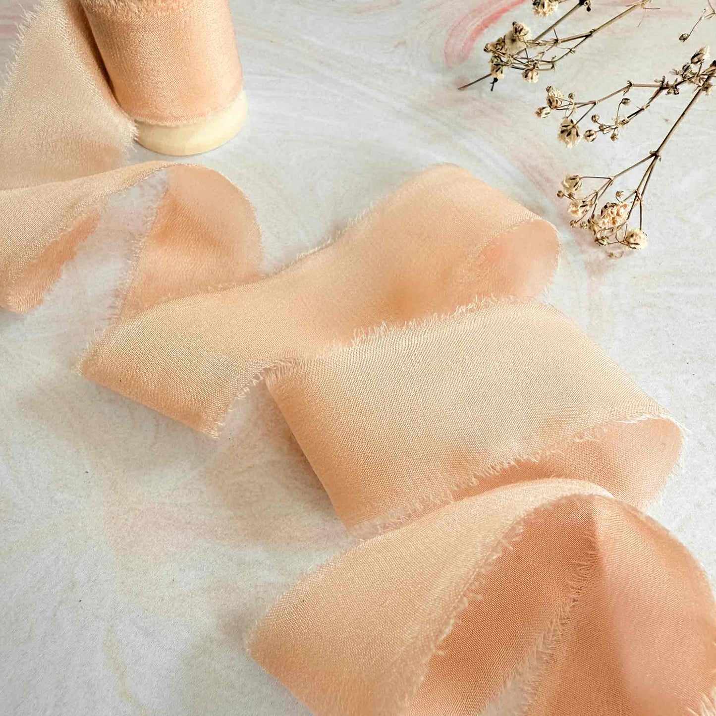 Peach colour silk ribbon with a frayed edge.  Sold on a wooden reel.