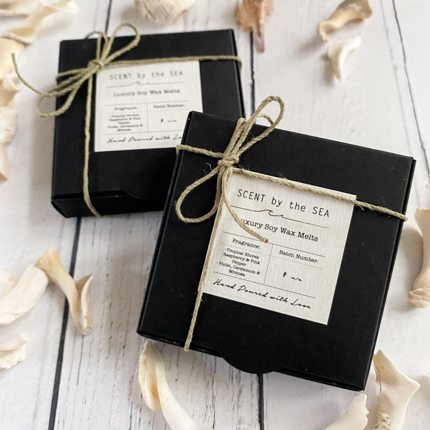 Two black boxes with twine bows and 'Scent by the Sea' labels on a white wooden surface.