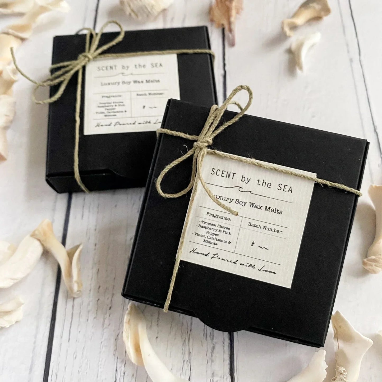 Two black boxes with twine bows and 'Scent by the Sea' labels on a white wooden surface.