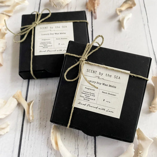 Two black boxes with twine bows and 'Scent by the Sea' labels on a white wooden surface.