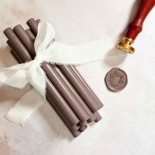 Set of gray sealing wax sticks with a white ribbon and a stamp on a light background