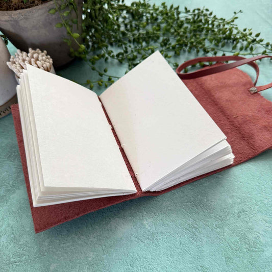 Open book with red cover on a light blue surface with greenery in the background