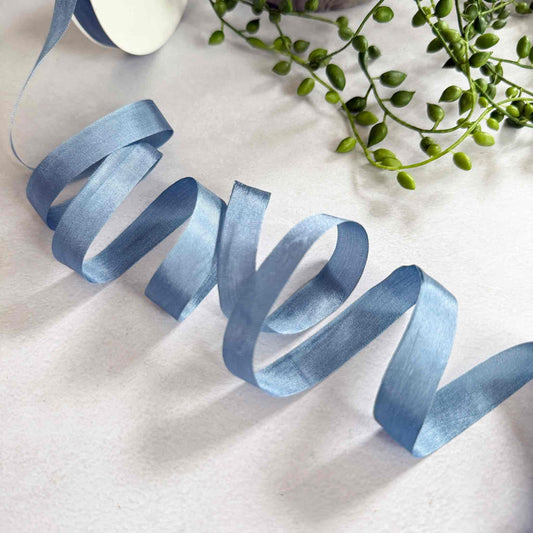 Blue ribbon on a white surface with green leaves in the background