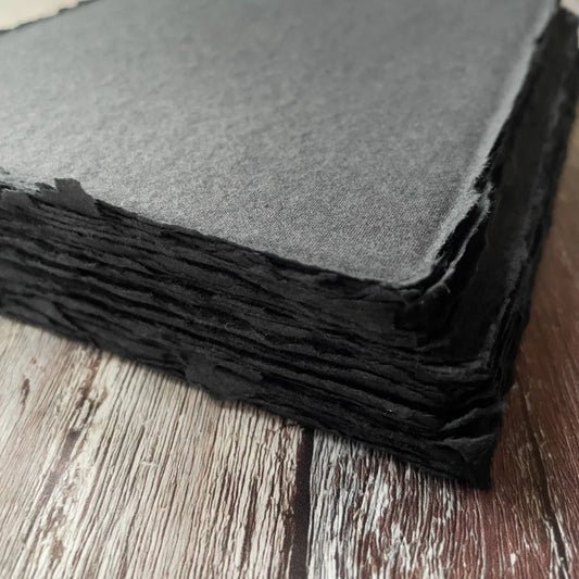 A stack of black handmade card with a textured surface and deckled edges on a wooden background.