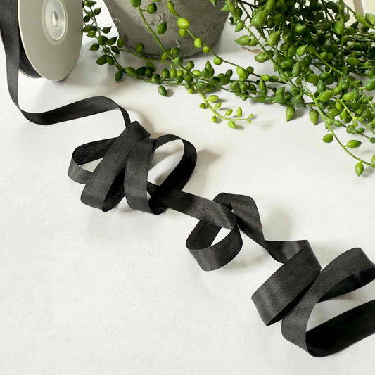 Black ribbon on a white surface with green leaves in the background