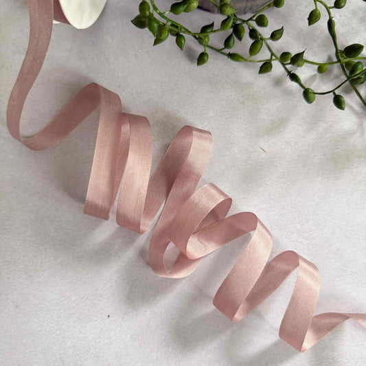 Pink ribbon on a light gray surface with green leaves in the background