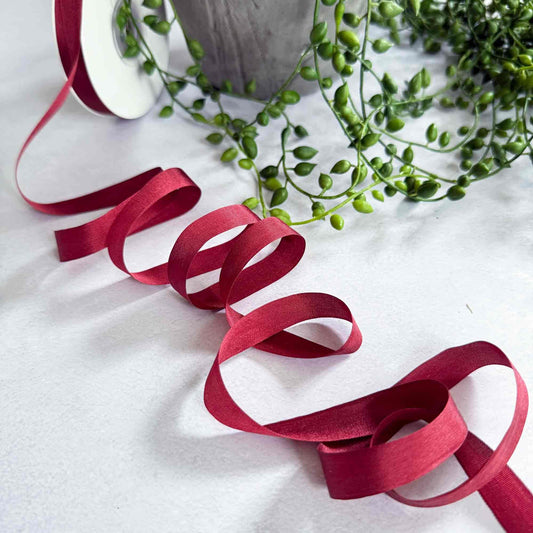 Red ribbon on a white surface with green leaves in the background