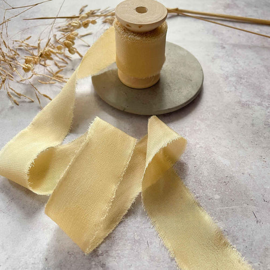 A spool of buttermilk-colored silk ribbon with a raw edge finish, presented on a wooden reel.
