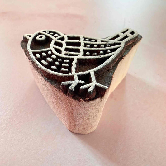 Wooden printing block with bird design on a pink background
