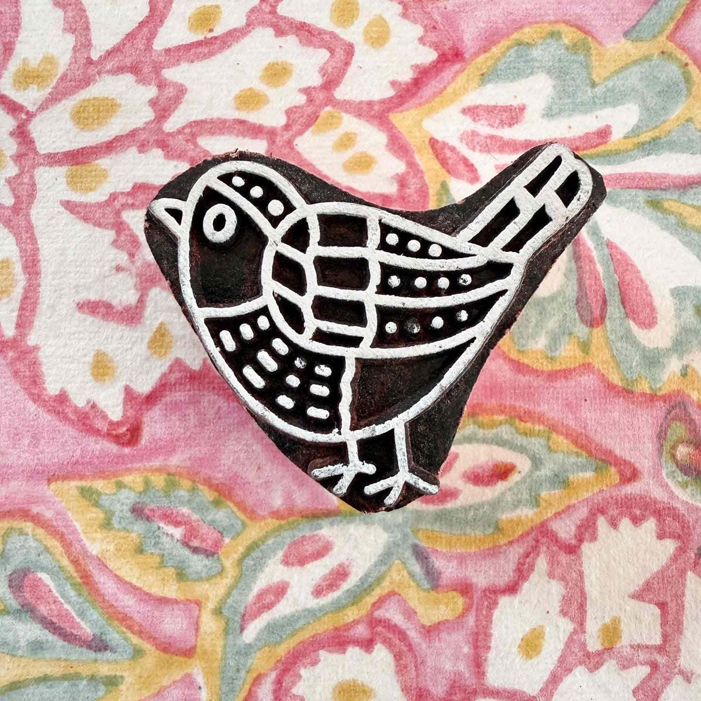 small wooden stamp with a bird design on a wood block pattern background
