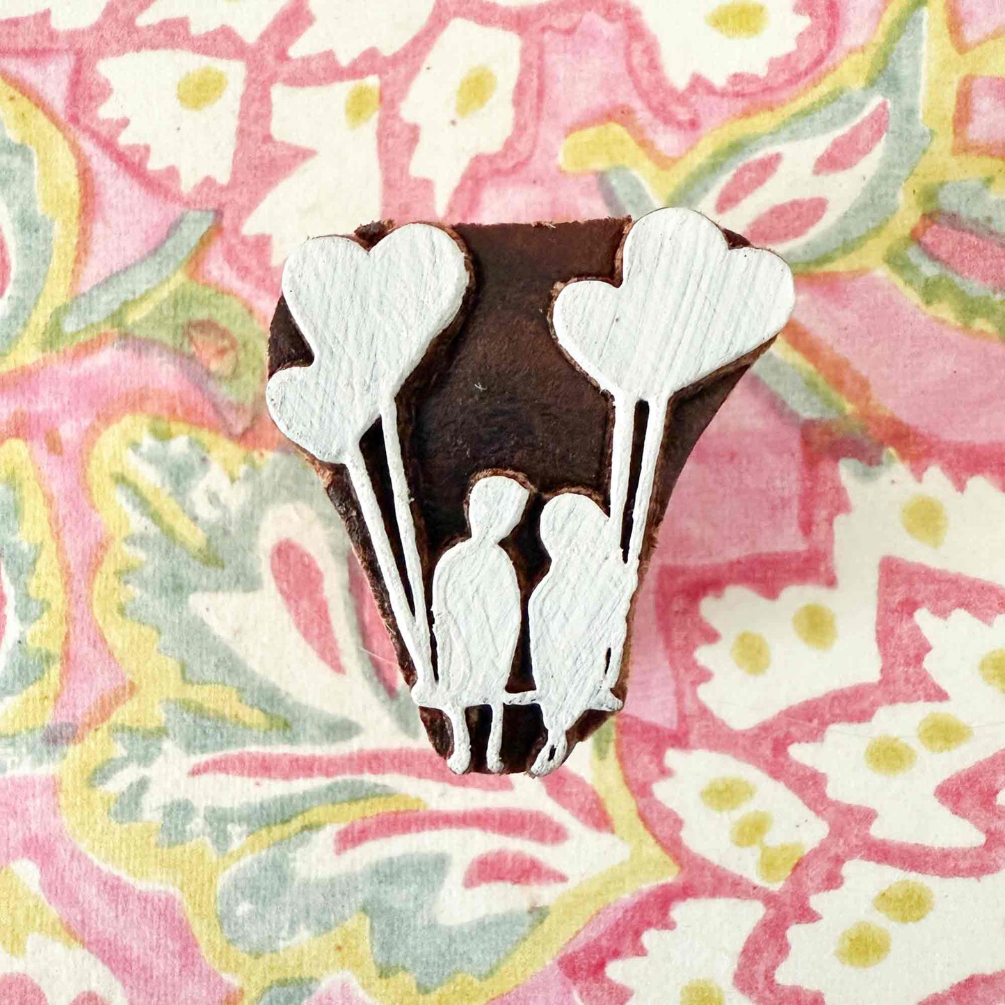 a wood block stamp with a boy and a girl holding heart shaped balloons