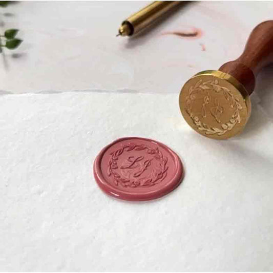 Wax seal and stamp on a white surface with a decorative design.