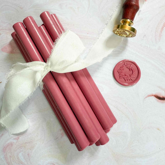 Pink sealing wax sticks with a white ribbon and a red wax seal on a marble surface
