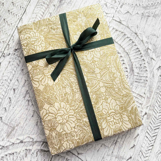 Gift box with gold floral pattern and green ribbon on a textured white surface
