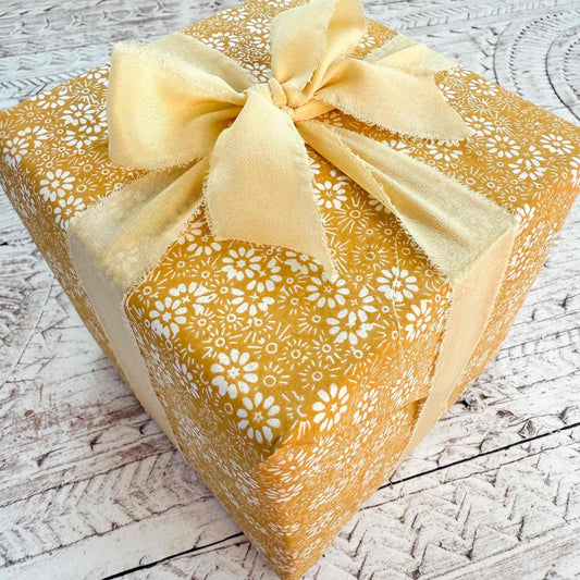 Gift box with yellow floral pattern and bow on a wooden surface