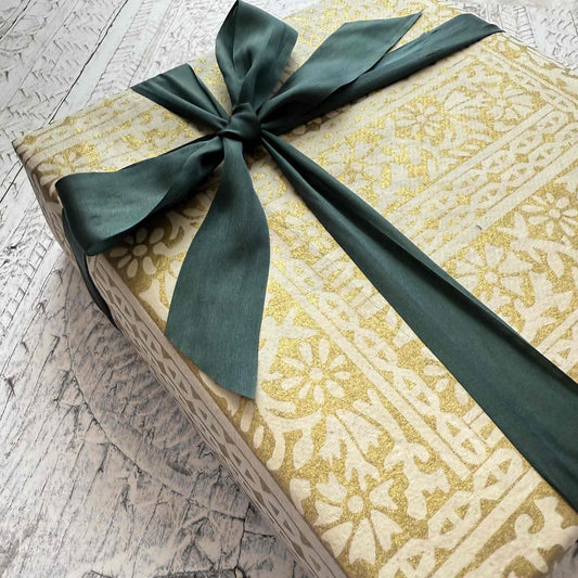 Gift box with gold pattern and green ribbon on a textured surface