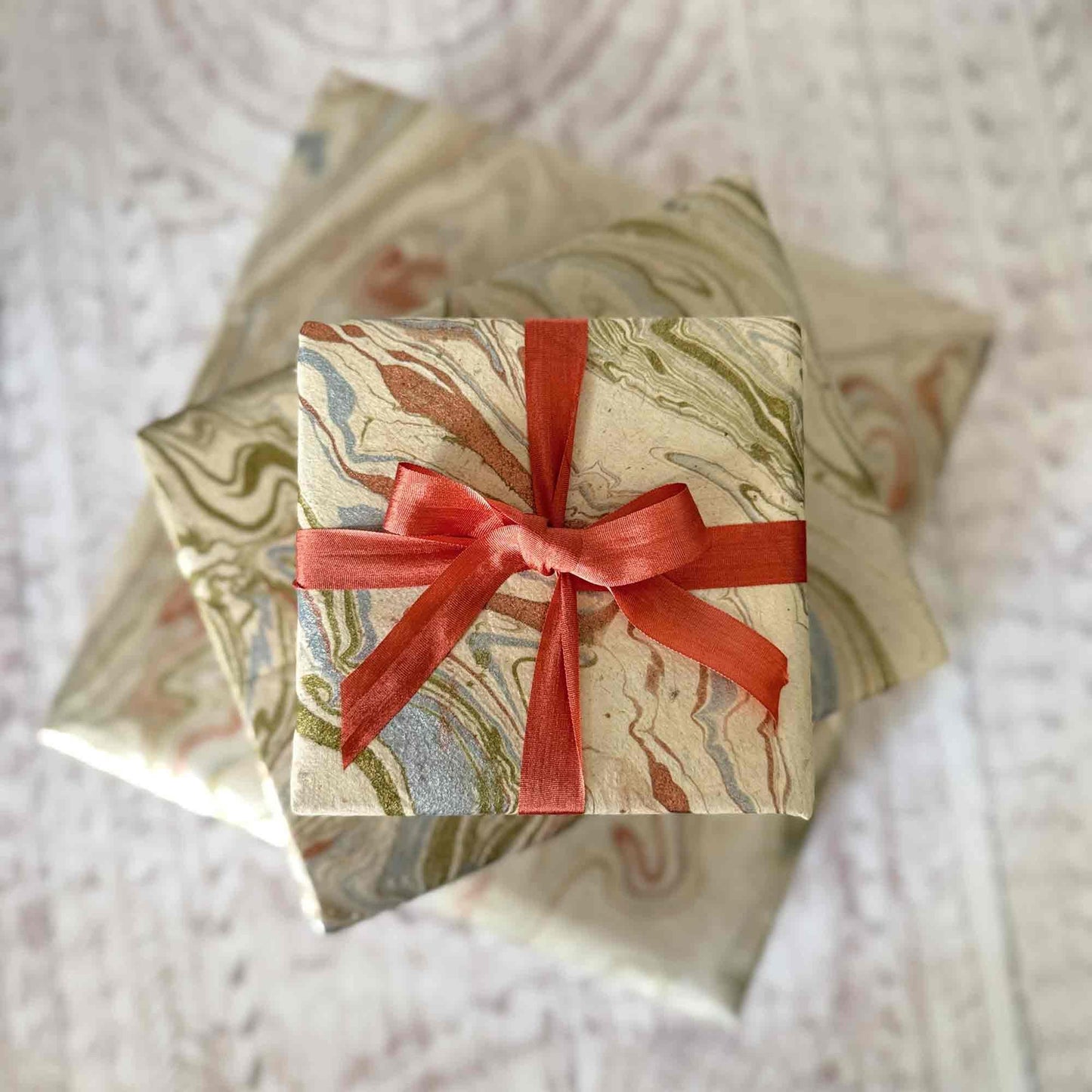Handmade Lokta paper gift wrap with hand-marbled pattern, wrapped gift boxes tied with orange ribbon – sustainable eco-friendly wrapping paper