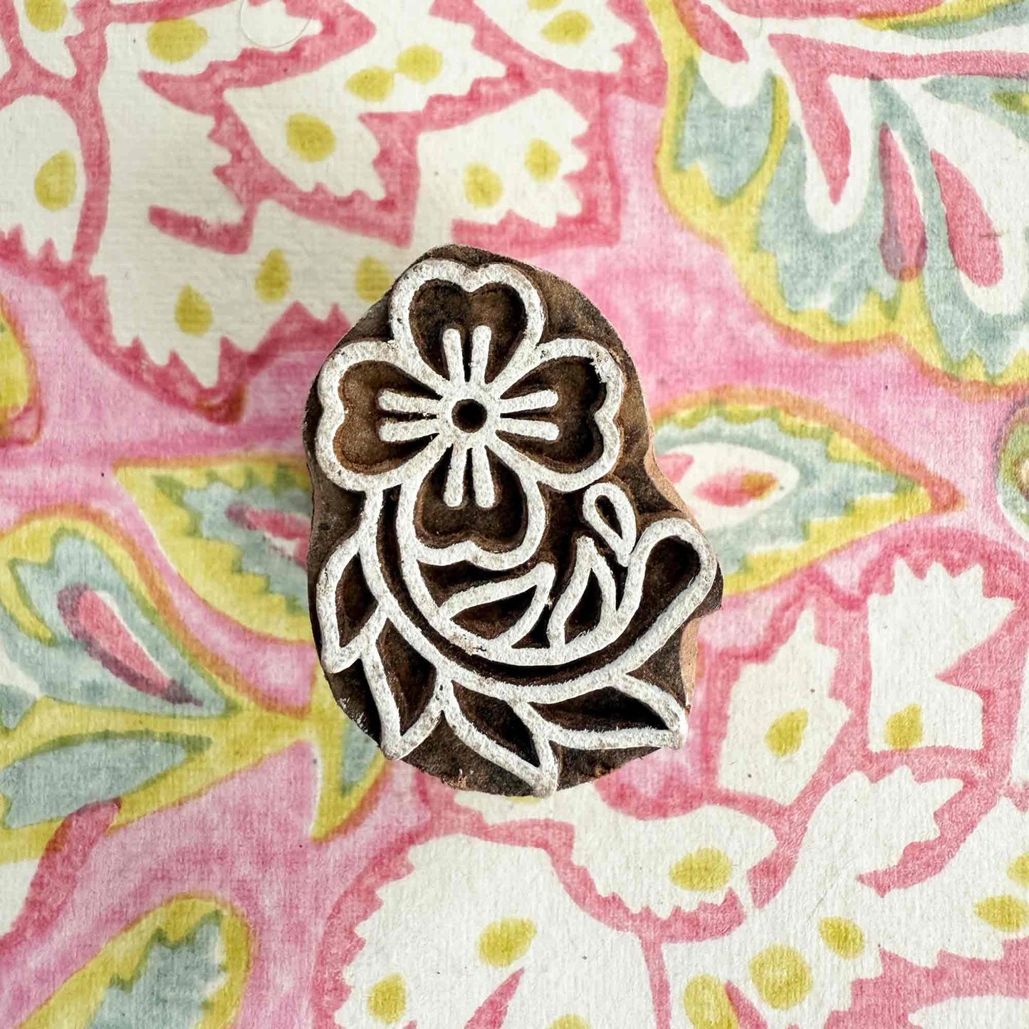 Decorative wooden stamp with floral design on a colorful fabric background