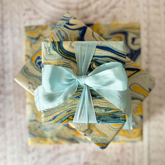 Top-down view of three nested gift boxes wrapped in unique marbled Lokta paper, finished with a soft light blue bow