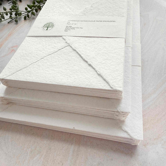 Stack of white envelopes with a visible brand logo on a light wooden surface.