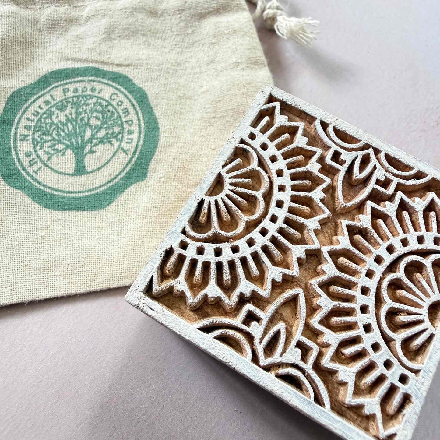 Wooden block with intricate floral design next to a branded gift bag