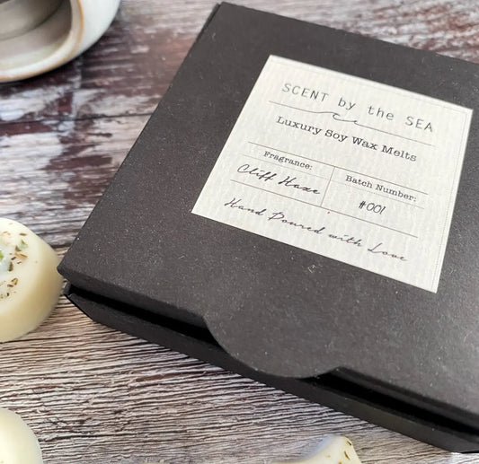 Box of luxury soy wax melts labeled 'Scent by the Sea' on a wooden surface.
