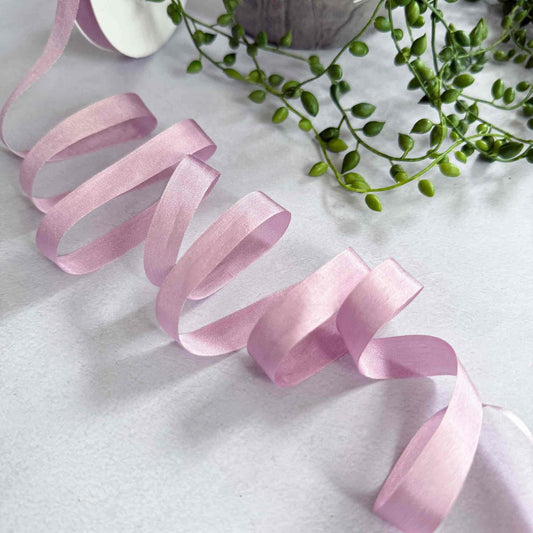 Pink ribbon on a white surface with green leaves in the background
