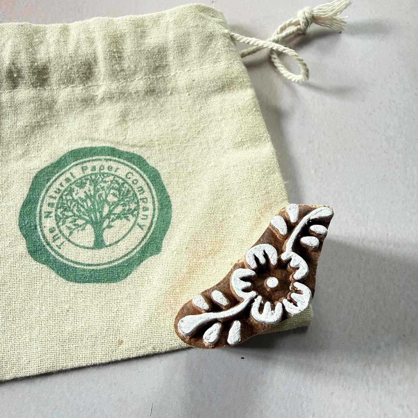 Decorative wooden stamp with floral design on a branded fabric pouch