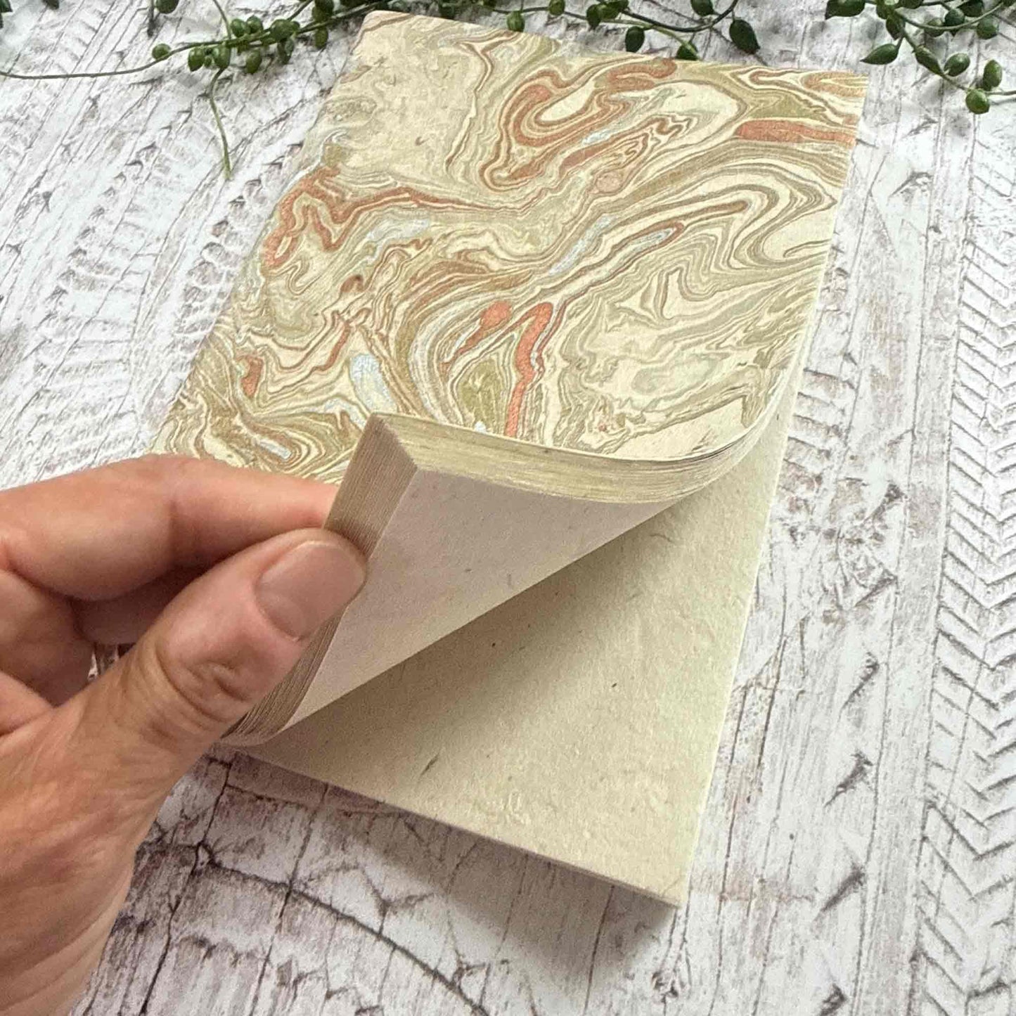 Hand opening a Midas Marble Lokta notebook, showing the soft natural texture of Lokta paper pages and the hand‑marbled gold and copper cover design