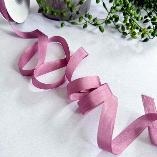 Pink ribbon on a white surface with green plants in the background
