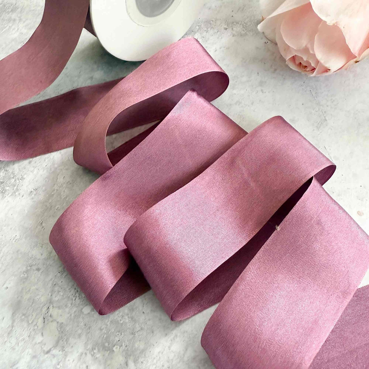 Pink ribbon on a light gray surface with a roll of tape and a pink rose.