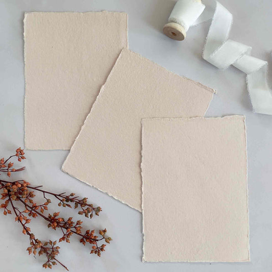 Stack of pink handmade cotton rag paper with a deckled edge, showing both the texture and color of the paper. A label on the side displays the brand and possibly other details.