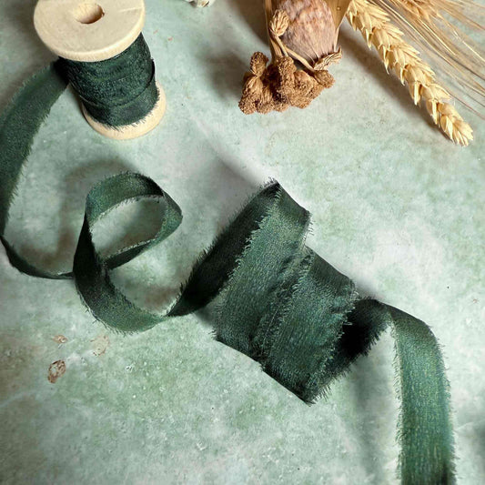 Green ribbon on a textured surface with a wooden spool and dried plant elements.