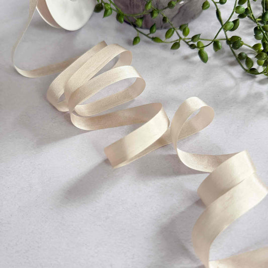 Beige ribbon on a light gray surface with green leaves in the background