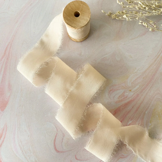 Fine silk ribbon with a frayed edge. Ivory silk ribbon on a wooden reel. By The Natural Paper Company.
