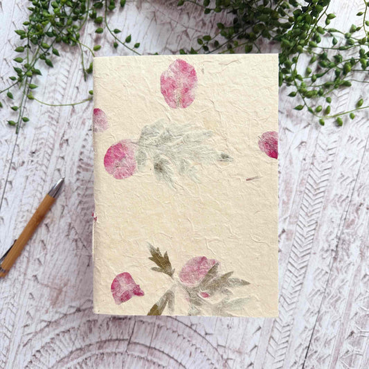 A5 botanical Lokta notebook — natural cream paper embedded with green Mugwort leaves and bright pink Bougainvillea petals, hand‑stitched and sustainable