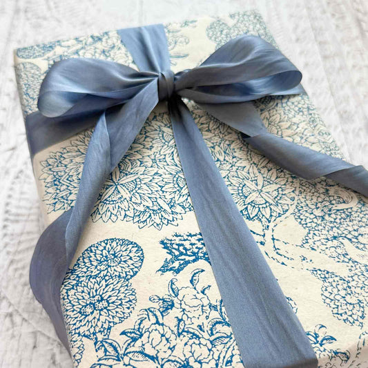 Gift wrapped in blue floral paper with a blue ribbon on a textured white background