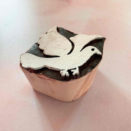 Wooden stamp with a dove design on a light pink background