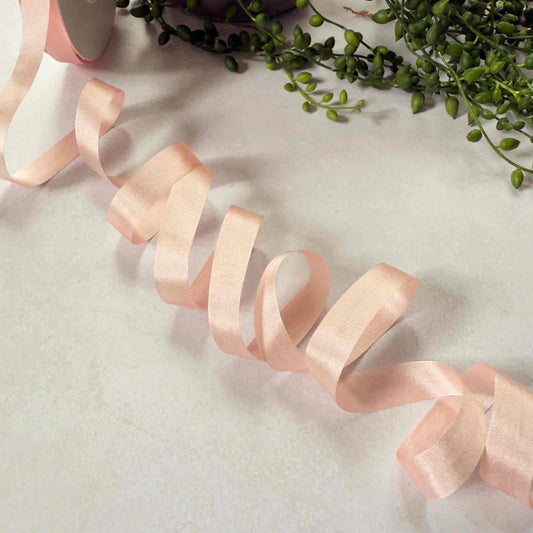 Pink ribbon on a textured surface with green leaves in the background