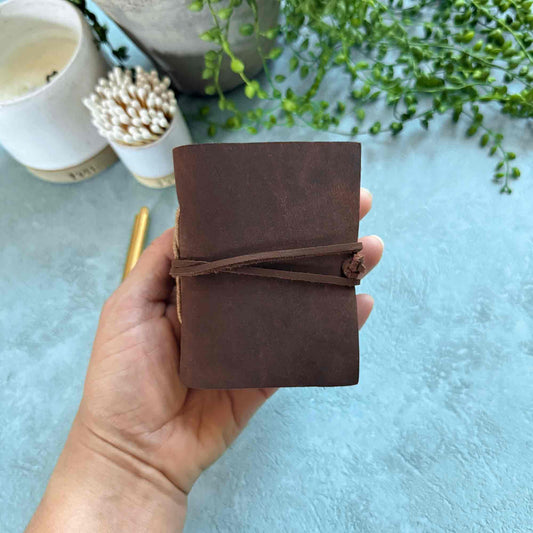 Hand holding a brown leather notebook with a light blue background