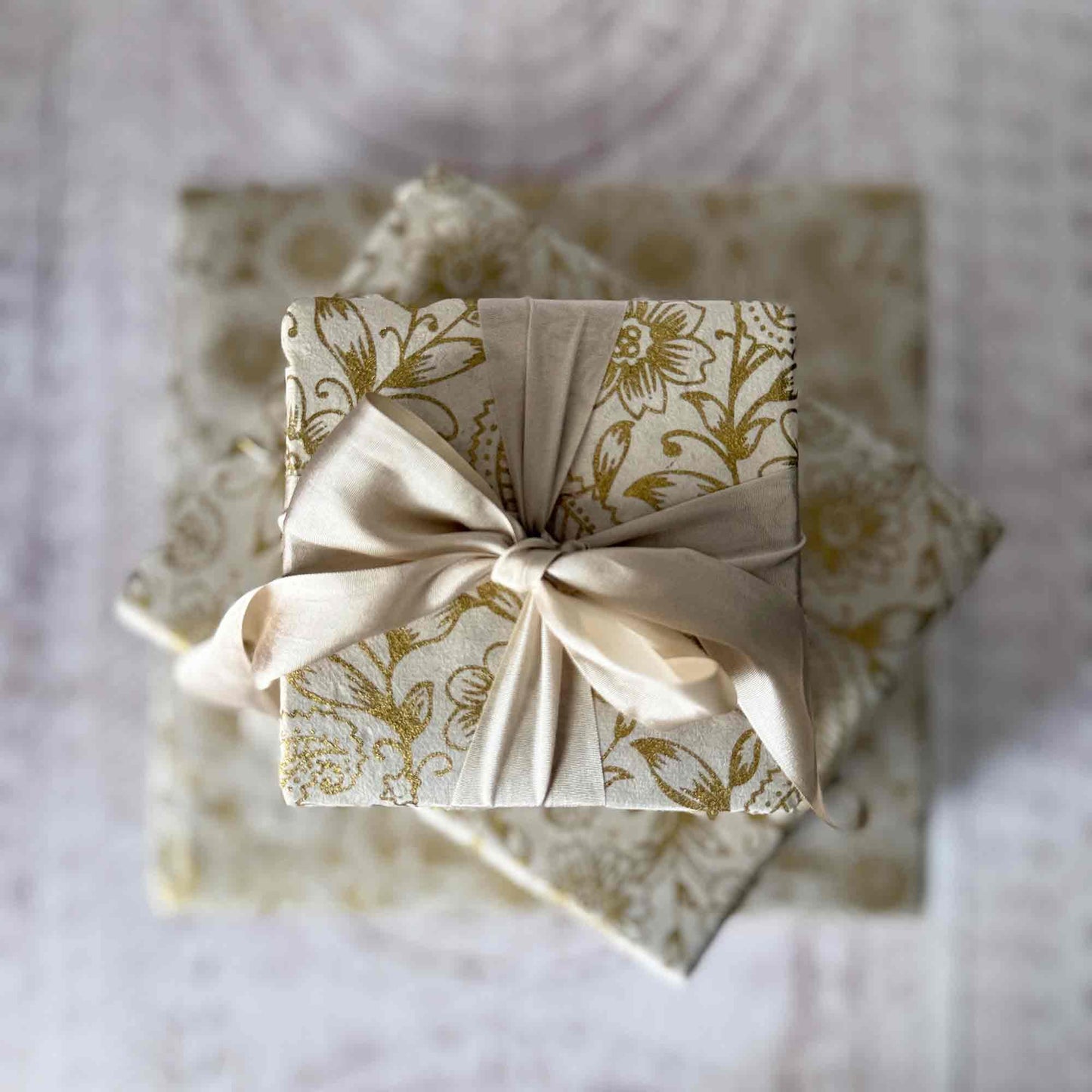 Top view of gift wrapped in Lokta paper with gold floral pattern and cream ribbon bow