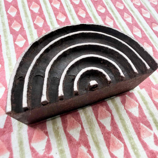 Hand-carved Rainbow Indian wood block stamp — semicircular concentric arches resting on block-printed fabric, traditional printing block close-up