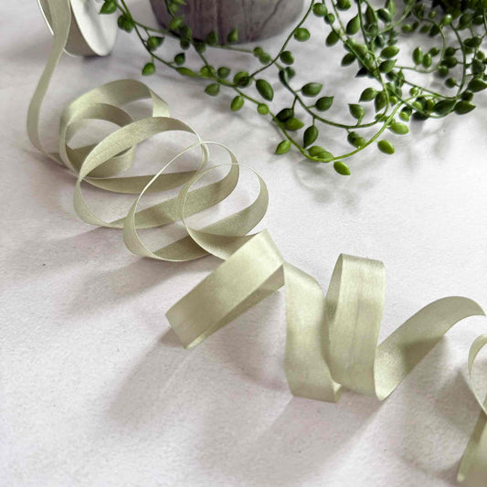 Light green ribbon on a white surface with green leaves in the background